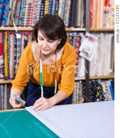 Female seller measuring and cutting off piece of textile 57125185