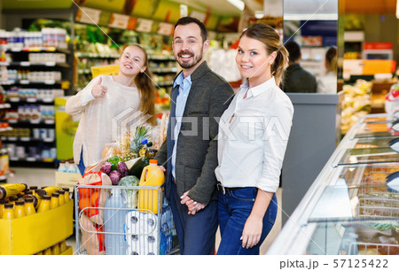 Family is standing with cart with products in the supermarket. Family is standing with cart with products in the supermarket. 57125422