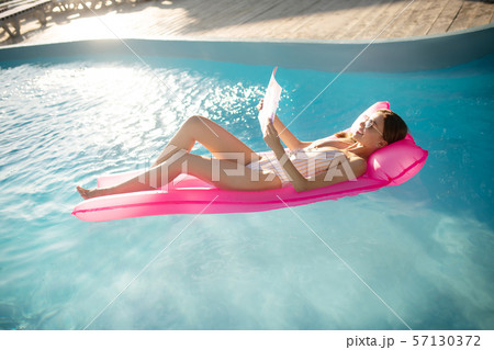 Woman reading magazine while lying on air bed in pool Woman reading magazine while lying on air bed in pool 57130372