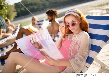 Woman wearing pink sunglasses reading beauty magazine Woman wearing pink sunglasses reading beauty magazine 57130626