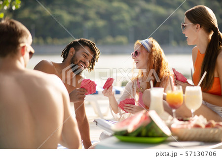 Friends laughing while playing cards sitting near river Friends laughing while playing cards sitting near river 57130706