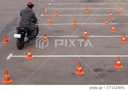 Man in helmet on motor-cycle making exercises on car-park among orange traffic cones Man in helmet on motor-cycle making exercises on car-park among orange traffic cones 57132691