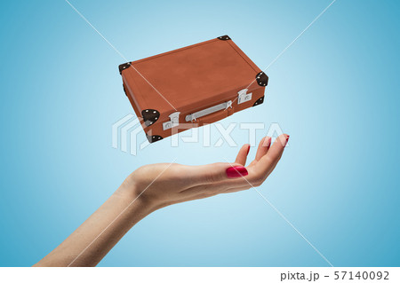 Closeup of woman's hand levitating brown travel case on light blue background. Closeup of woman's hand levitating brown travel case on light blue background. 57140092