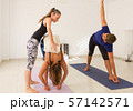 Woman in yoga studio adjusts student in Mysore style ashtanga class. Female teacher with young yogis. Man in utthita trikonasana, known as extended triangle pose. Healthy workout, exercise concepts 57142571