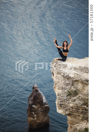 Beautiful slim woman practices yoga and pilates on the cliff of mountain with the sea view. Sportive 57161300