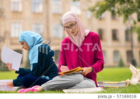 Muslim student wearing glasses studying hard near friend Muslim student wearing glasses studying hard near friend 57166016