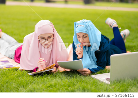 Two muslim students sitting on grass and preparing to exam 57166115
