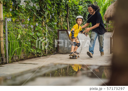 Athletic boy learns to skateboard with asian trainer in a skate park. Children education, sports Athletic boy learns to skateboard with asian trainer in a skate park. Children education, sports 57173297