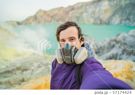 Young man tourist makes a selfie standing at the edge of the crater of the Ijen volcano or Kawah 57174424