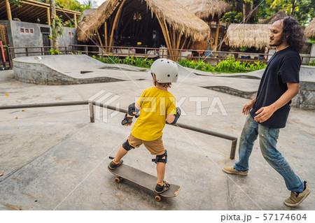 Athletic boy learns to skateboard with a trainer in a skate park. Children education, sports 57174604