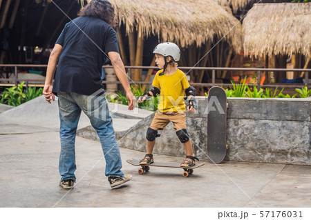 Athletic boy learns to skateboard with a trainer in a skate park. Children education, sports Athletic boy learns to skateboard with a trainer in a skate park. Children education, sports 57176031