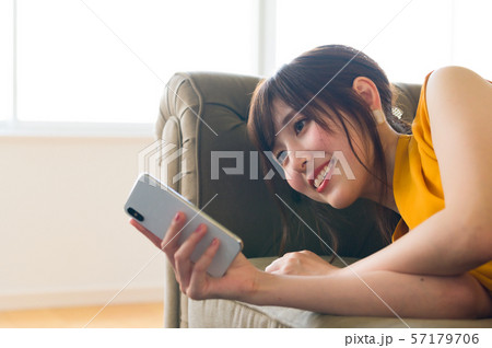 ソファに寝転んでスマホを操作する若い女性 57179706