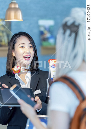 外国人観光客にタブレットで宿泊情報を案内する笑顔の女性観光ガイド受付嬢 57190428