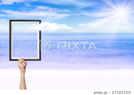 Abstract image of Hand holding picture frame with beautiful seascape view in background. Abstract image of Hand holding picture frame with beautiful seascape view in background. 57203250