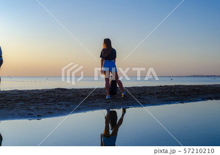 A girl with a backpack stands on the beach and sees off the sunset. A girl with a backpack stands on the beach and sees off the sunset. 57210210