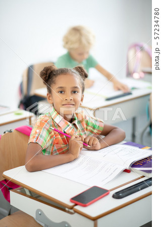 Dark-eyed girl holding pencil while sitting at the desk 57234780