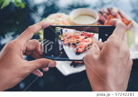 Camera eats first concept: man taking pictures food on the table with smartphone for social media Camera eats first concept: man taking pictures food on the table with smartphone for social media 57242281