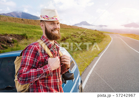 Portrait of a bearded happy smiling traveler hipster with a backpack in a plaid shirt and a hat next 57242967