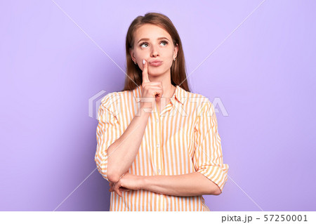 Dreamy pretty female keeps index finger near lips, looking somewhere above 57250001