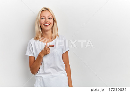 Happy charming young woman has joyful expression, points with finger aside 57250025