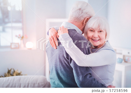 Beaming retired woman feeling happy hugging her grey-haired husband Beaming retired woman feeling happy hugging her grey-haired husband 57258596