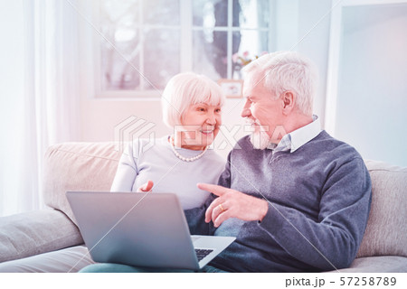 Watching film. Modern retired couple feeling involved in watching film on their laptop while sitting Watching film. Modern retired couple feeling involved in watching film on their laptop while sitting 57258789