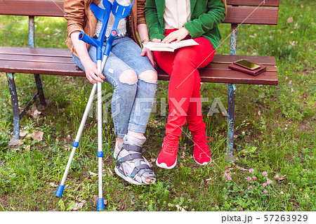 Two friends reading a book in the park, one has a broken foot 57263929