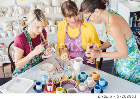 Teacher showing women in workshop how to paint self-made dishes Teacher showing women in workshop how to paint self-made dishes 57263953