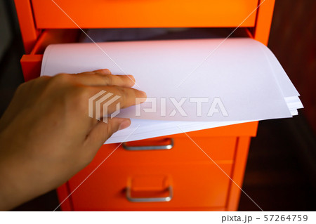 Woman's hand pick up white papers for write letter, Filing cabinet with open drawer, Orange metal colour, Administration and storage concept, closeup & Macro shot, Selective focus Woman's hand pick up white papers for write letter, Filing cabinet with open drawer, Orange metal colour, Administration and storage concept, closeup & Macro shot, Selective focus 57264759