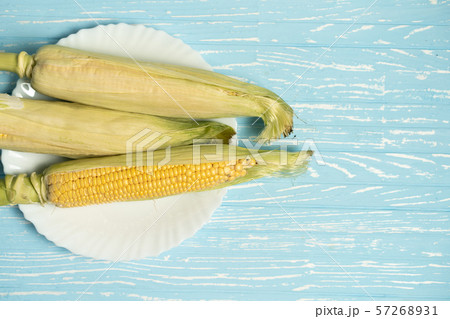 Corn cob with green leaves lies on white plate 57268931