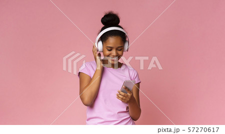 Young black girl listening music on smartphone, using wireless headphones Young black girl listening music on smartphone, using wireless headphones 57270617