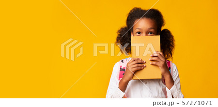 African American Schoolgirl Covering Face With Book, Yellow Background African American Schoolgirl Covering Face With Book, Yellow Background 57271071