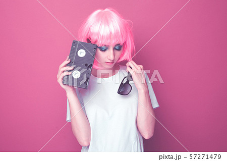 90s style concept. Young woman with pink hail holding glasses and cassette standing in the pink 57271479