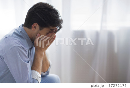 Frustrated Lonely Man Covering Face With Hands Sitting Against Window 57272175