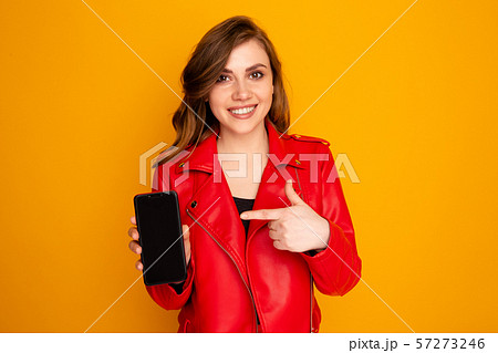 Closeup photo of girl pointing black phone isolated over the yellow background. 57273246