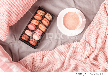 Bed with pink knitted plaid, coffee and macaroons. 57282148