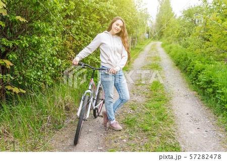 Young woman riding bicycle in summer city park outdoors. Active people. Hipster girl relax and rider Young woman riding bicycle in summer city park outdoors. Active people. Hipster girl relax and rider 57282478