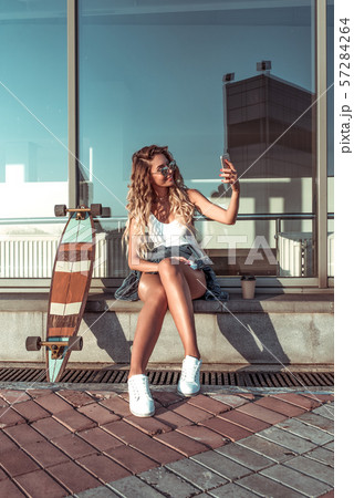 Beautiful girl with glasses, sitting near building, in summer in city, holding cup of coffee 57284264