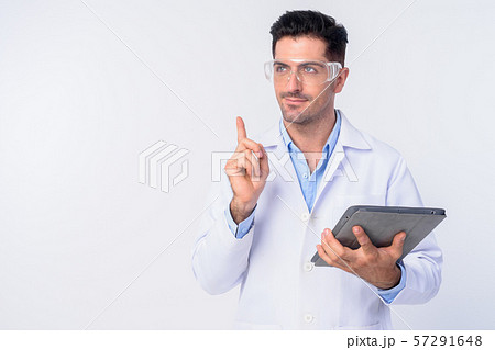 Young handsome man doctor with protective glasses pointing up while holding digital tablet Young handsome man doctor with protective glasses pointing up while holding digital tablet 57291648