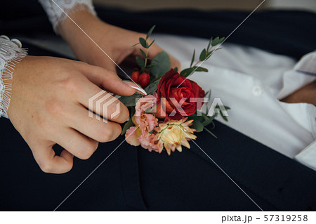 Hands of bride outdoors. Bride corrects boutonniere on groom's wedding jacket 57319258