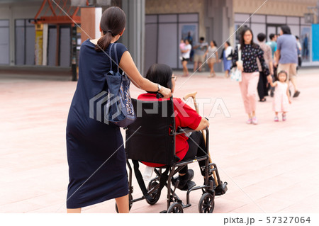 Daughter pushing her mother in wheelchair walking along the shopping mall. Daughter pushing her mother in wheelchair walking along the shopping mall. 57327064