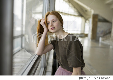 Redhead young woman leaning against window 57348582