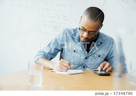 Man using smart phone while writing on note pad Man using smart phone while writing on note pad 57348790