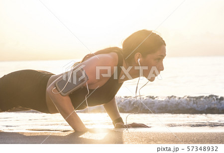 Woman wearing headphones doing push-up on beach Woman wearing headphones doing push-up on beach 57348932