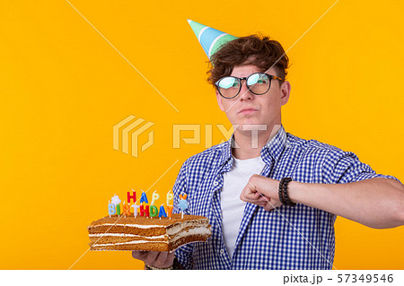 Portrait of a funny positive guy with a paper cap and glasses holding a congratulatory cake in his 57349546