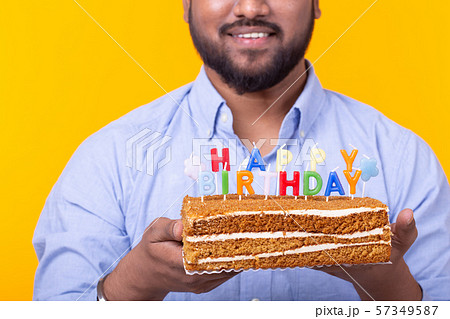 Close-up of funny young indian guy with a cap and a homemade cake in his hands posing on a yellow 57349587