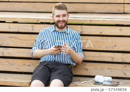 Happy young male hipster student with a mustache and beard writing sms message to his friends Happy young male hipster student with a mustache and beard writing sms message to his friends 57349656