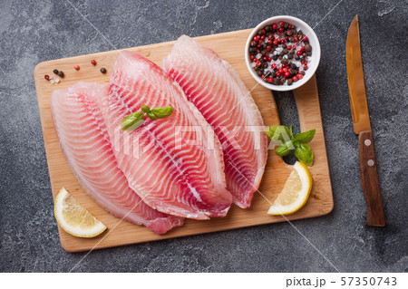 Raw fish fillet of tilapia on a cutting Board with lemon and spices. Dark table with copy space. 57350743