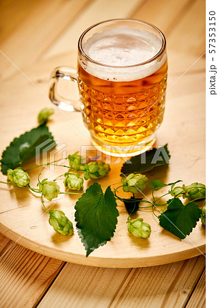 Large pint of beer with foam and sprigs of hops on wooden table 57353150