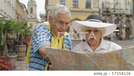 Senior male and female tourists standing with a map in hands looking for route Senior male and female tourists standing with a map in hands looking for route 57358126